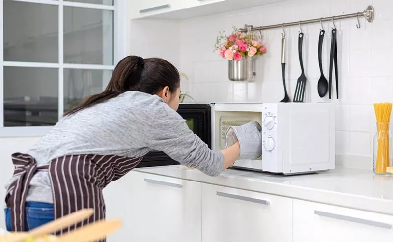 Une jeune fille utilise un gant de cuisine pour retirer le bocal stérilisé au micro onde.
